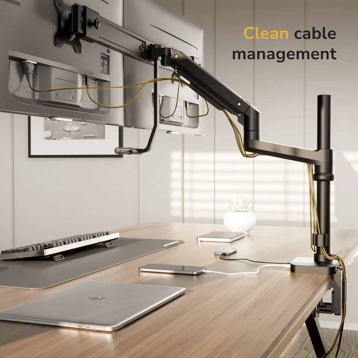 A modern workspace displays two monitors on the Mount-It! Dual Monitor Mount with Pole and Crossbar, featuring organized cables. A keyboard, mouse, laptop, and smartphone rest on a wooden desk under daylight. Text reads, “Clean cable management.”.