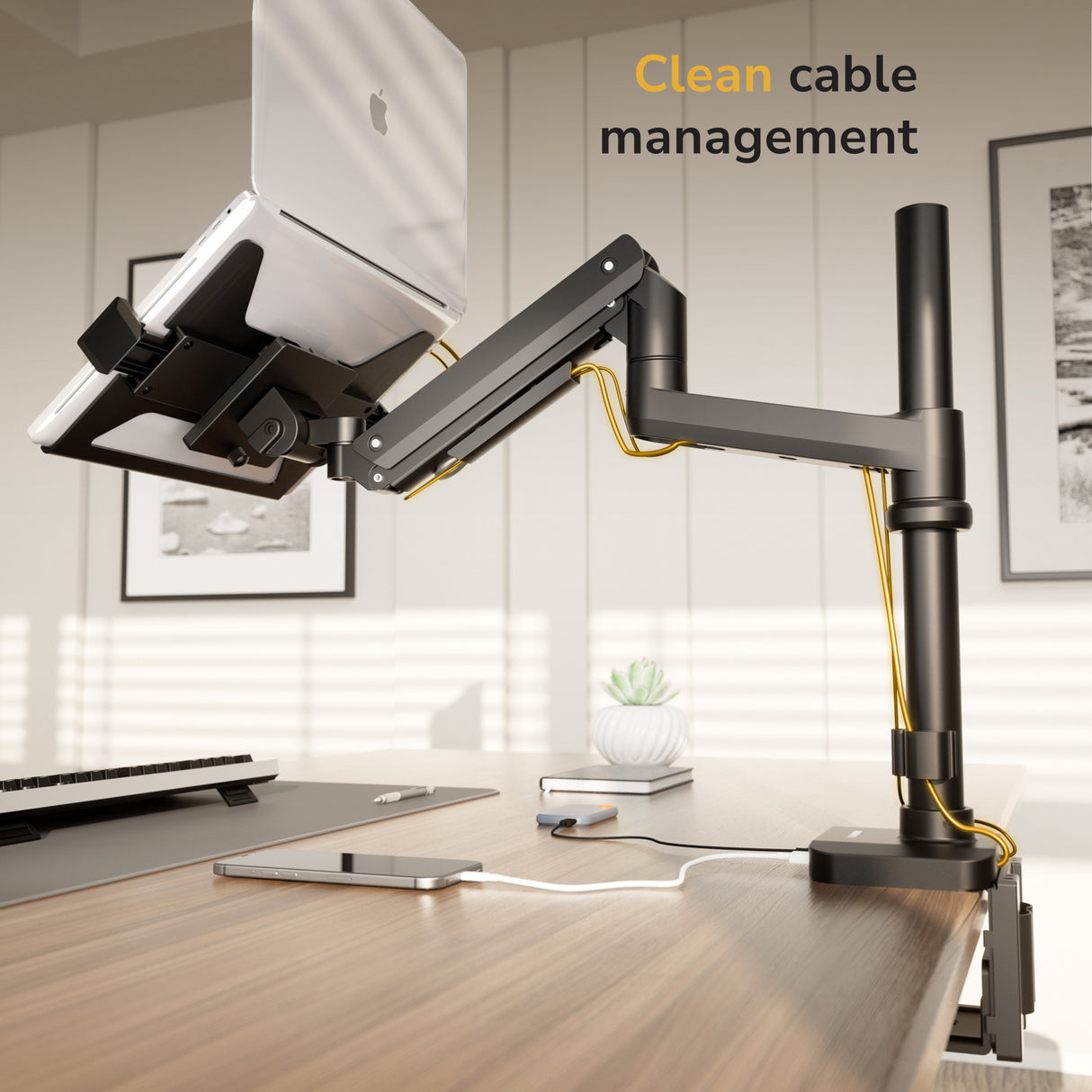 Modern desk setup featuring a Mount-It! Laptop Mount with Pole and Gas Spring Arm, yellow cables neatly organized along the adjustable arm. A keyboard, phone, and plant rest on the wooden desk. Text reads “Clean cable management.”.