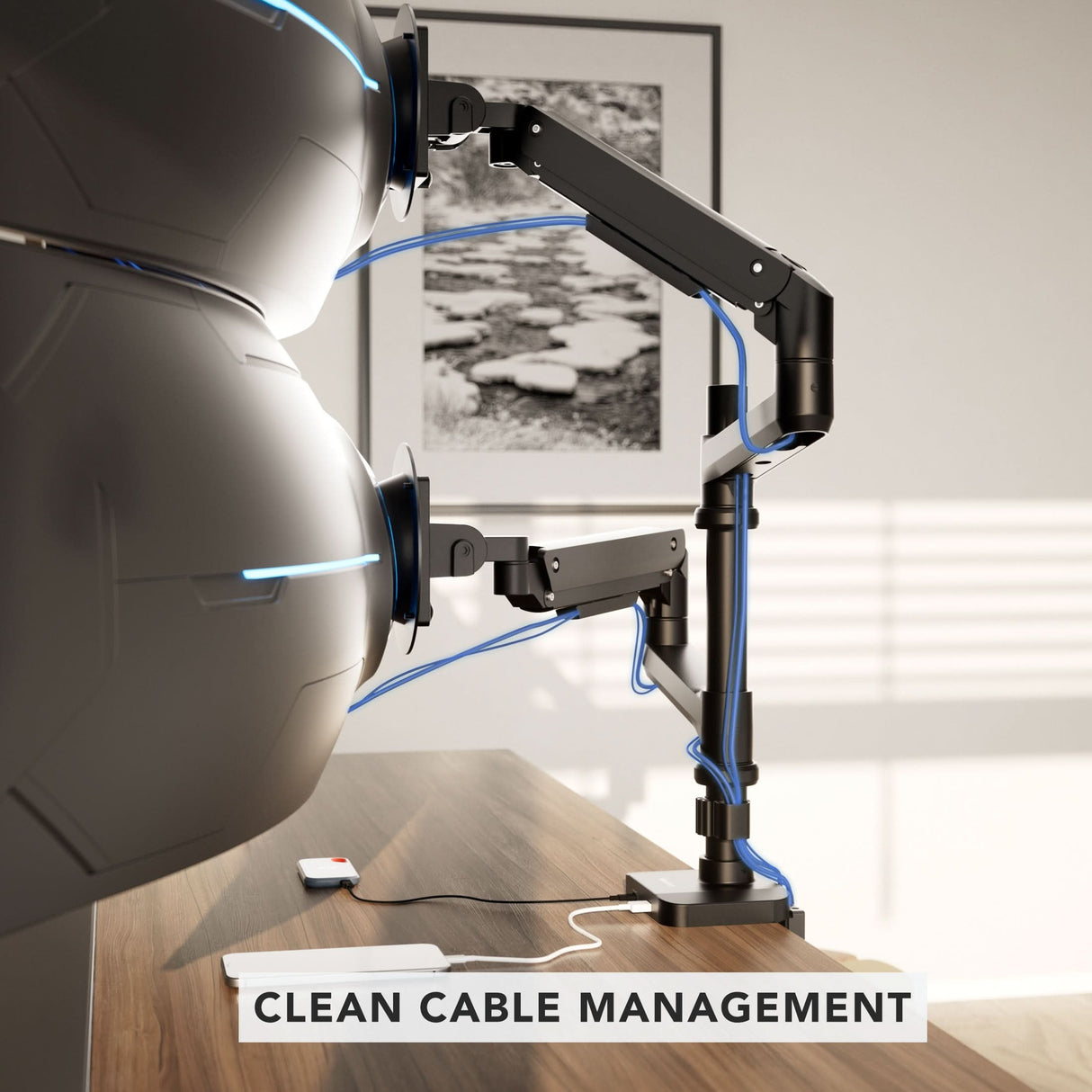 Heavy-Duty Dual Stacking Monitor Mount with Pole & Gas Spring Arms A wooden desk displays the Mount-It! Heavy-Duty Dual Stacking Monitor Mount with Pole & Gas Spring Arms, offering full motion flexibility and organized blue cables. A "CLEAN CABLE MANAGEMENT" label is seen, with black and white art on the wall behind.
