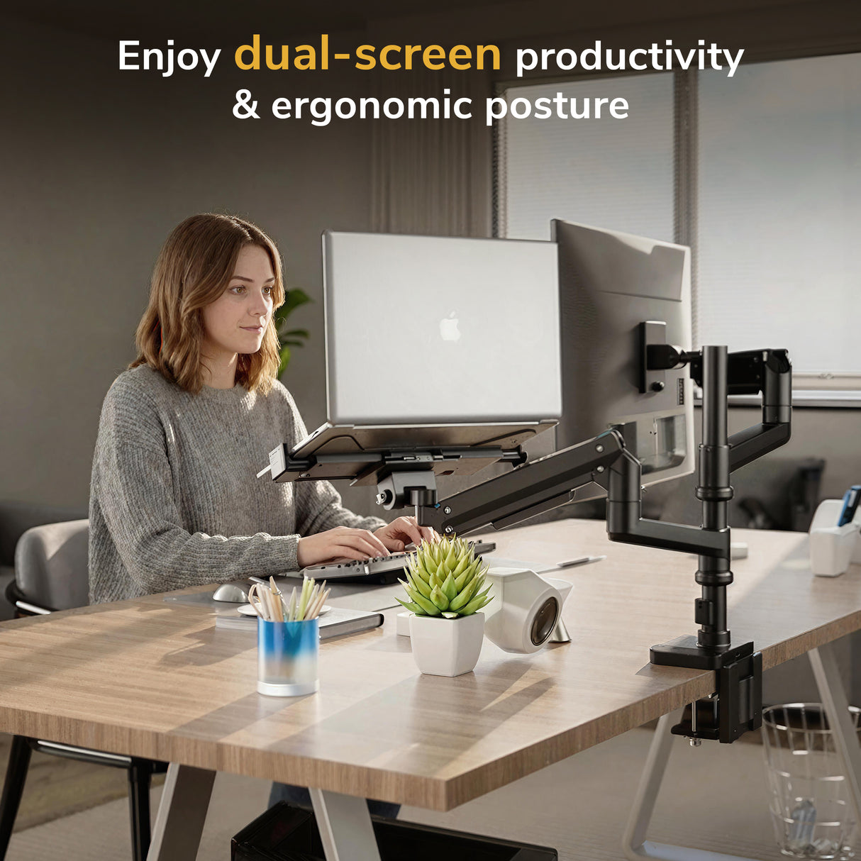 A woman works at a tidy desk using the Mount-It! Heavy-Duty Monitor and Laptop Mount with Pole and Gas Spring Arms, promoting ergonomic posture and dual-screen productivity. The workspace features plants and stationery for an organized feel.