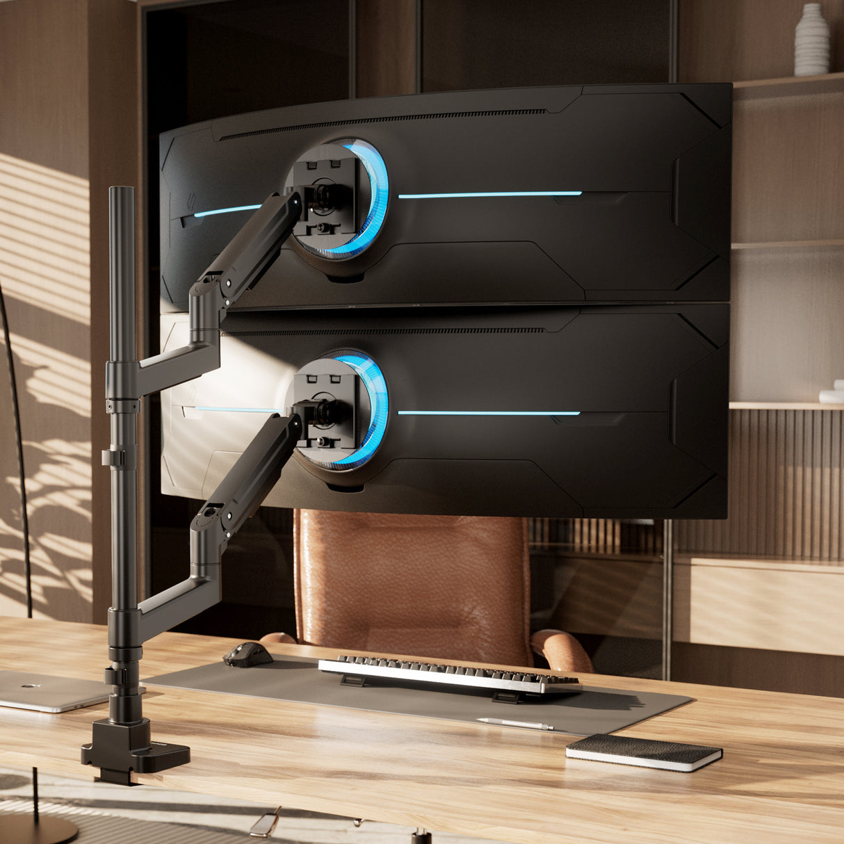 Two large curved monitors are vertically mounted on the Mount-It! Heavy-Duty Dual Stacking Monitor Mount above a modern wooden desk with a keyboard, mouse, laptop, and chair in a bright office.