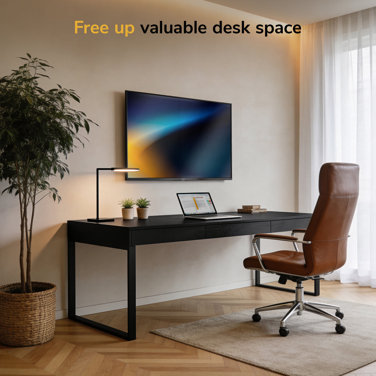Modern home office featuring a Mount-It! Low-Profile TV Wall Mount supporting a monitor, black desk, brown leather chair, laptop, desk lamp, and potted plant. Sunlight streams in. Text: “Free up valuable desk space.”.