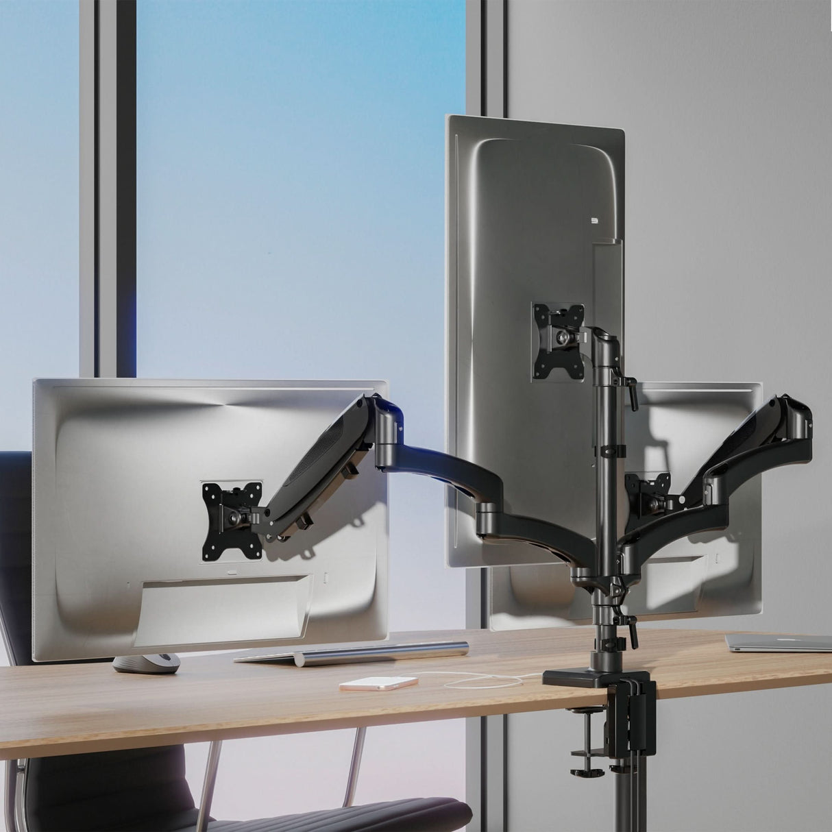Triple Monitor Mount with Gas Spring Arms and USB Ports Triple Monitor Mount with Gas Spring Arms and USB Ports installed on a desk near a window, featuring three adjustable monitors held by sturdy gas spring arms allowing tilt, swivel, and rotation for ergonomic comfort, with the mount clamped securely to the edge of the desk, designed to support multiple screens while saving space and offering integrated USB connectivity for device charging and accessory connection.