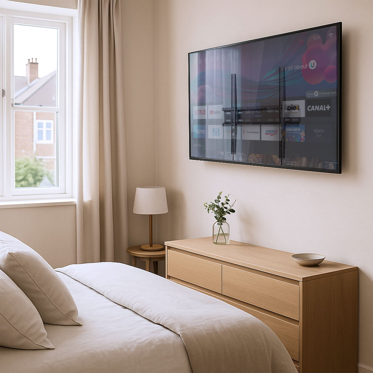 Low Profile Slim TV Wall Mount Fixed TV Bracket Modern bedroom featuring a flat-panel TV mounted with the Mount-It! Low Profile Slim TV Wall Mount Fixed TV Bracket, holding a 32-55 inch screen securely just over one inch from the wall for a sleek, space-saving look, with a light wood dresser, minimal decor, and natural light from a large window enhancing the clean, contemporary setup.