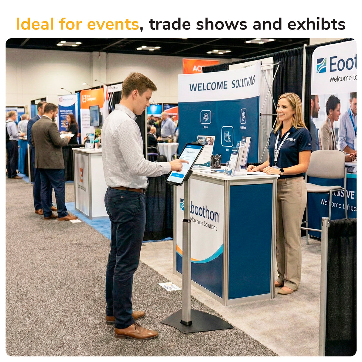 A man uses the Mount-It! Secure Universal Tablet Floor Stand with Lock at a trade show booth while a woman smiles behind the counter. Other booths and attendees are in the background. Text reads, Ideal for events, trade shows, and exhibits.