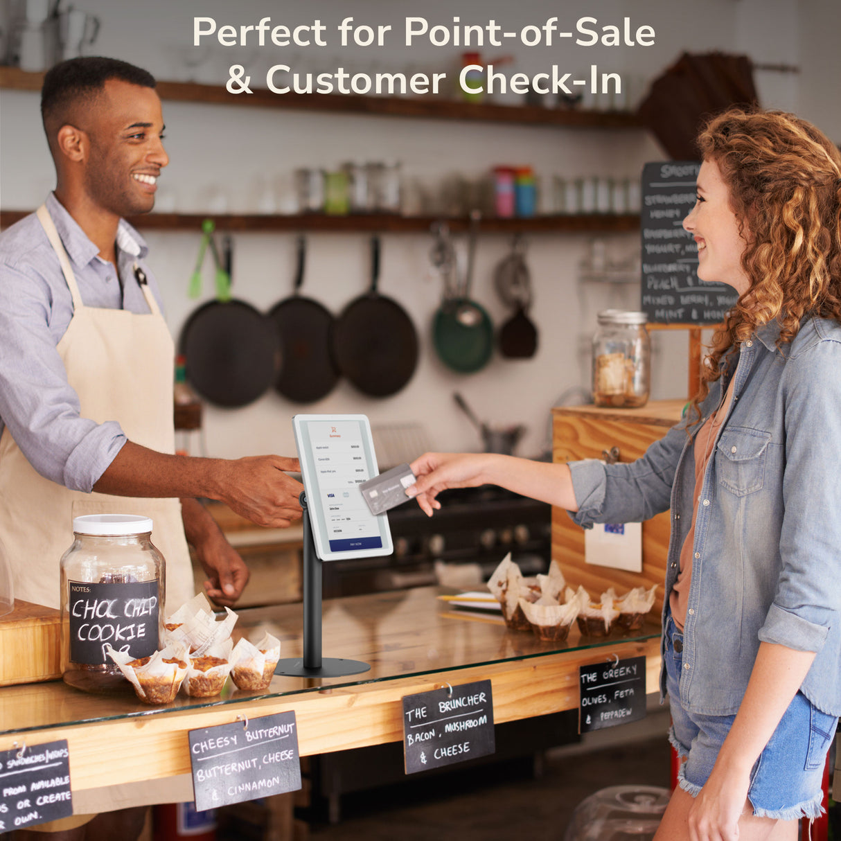 Universal Anti-Theft Tablet Countertop Stand A smiling barista hands a receipt to a customer tapping a card on a touchscreen secured by the Mount-It! Universal Anti-Theft Tablet Countertop Stand, with baked goods and a “Perfect for Point-of-Sale & Customer Check-In” sign nearby.