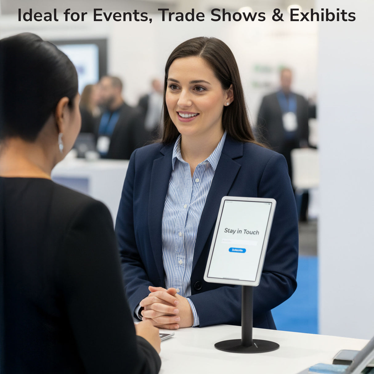 Universal Anti-Theft Tablet Countertop Stand At a trade show booth, a businesswoman chats with a visitor as the Mount-It! Universal Anti-Theft Tablet Countertop Stand displays a “Stay in Touch” message. Text above: Ideal for Events, Trade Shows & Exhibits.