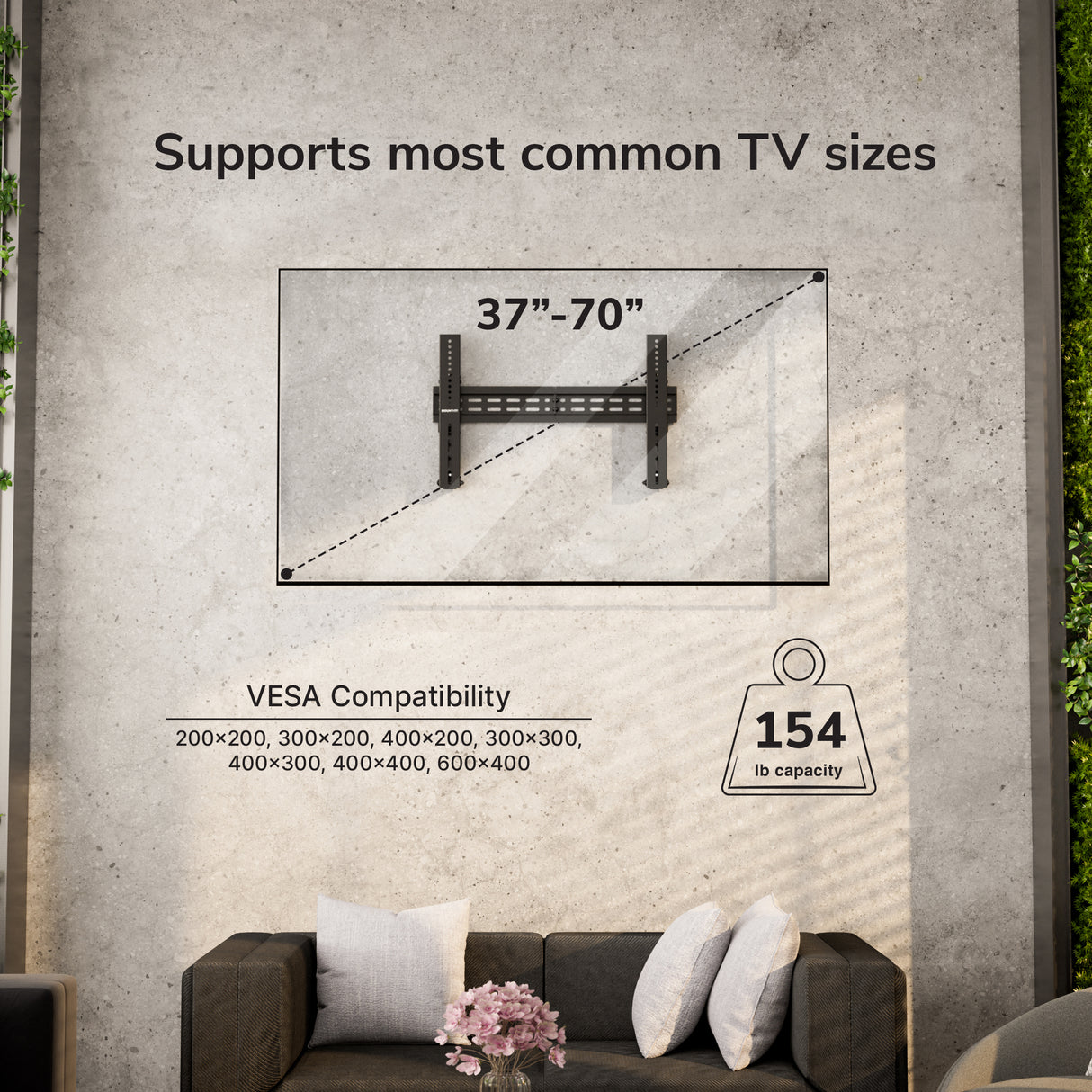 The Mount-It! Pop-Out Video Wall Mount fits 37–70" TVs, supports up to 154 lbs, and allows precise alignment with various VESA sizes. Shown mounted above a gray couch with white pillows and a pink flower arrangement.