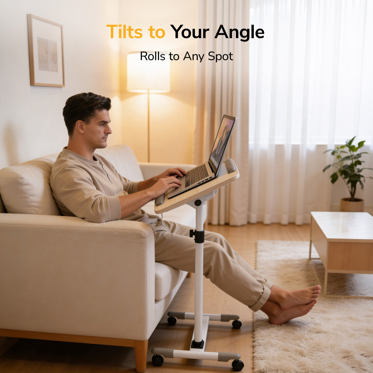 A man uses a laptop on the Mount-It! Height Adjustable Rolling Laptop Cart in a bright room with natural light, wall art, and white curtains. Text: Tilts to Your Angle. Rolls to Any Spot.