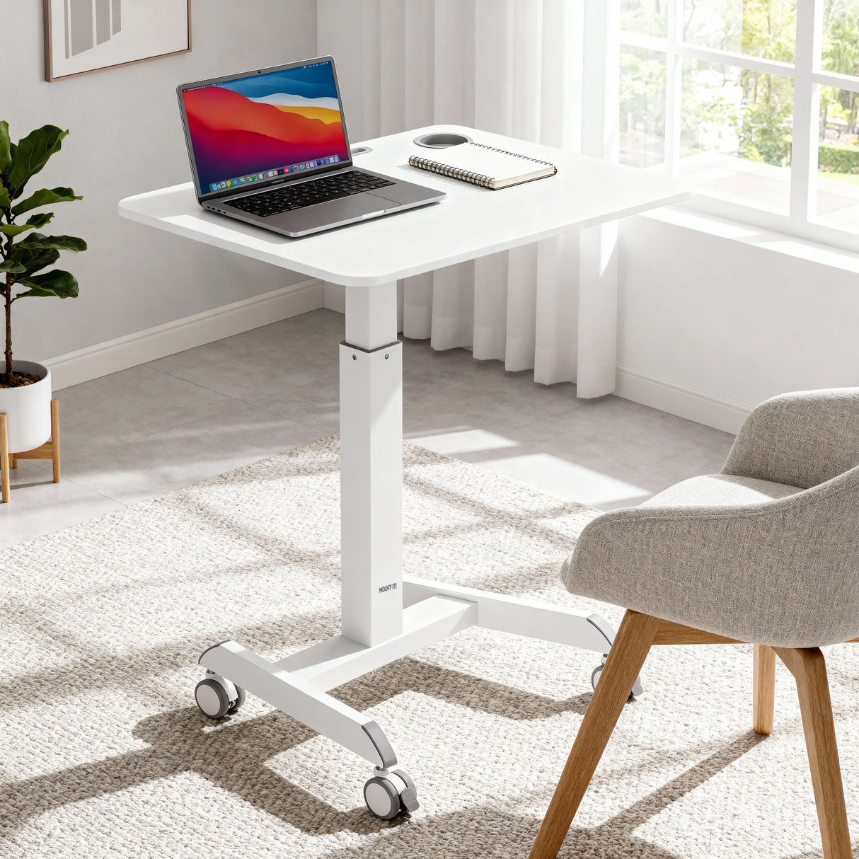 Sit-Stand Mobile Laptop Cart The Mount-It! Sit-Stand Mobile Laptop Cart, in white and height adjustable with wheels, holds a laptop and mouse. It stands in a bright room with large windows, white curtains, a light rug, and a gray cushioned chair with wooden legs.