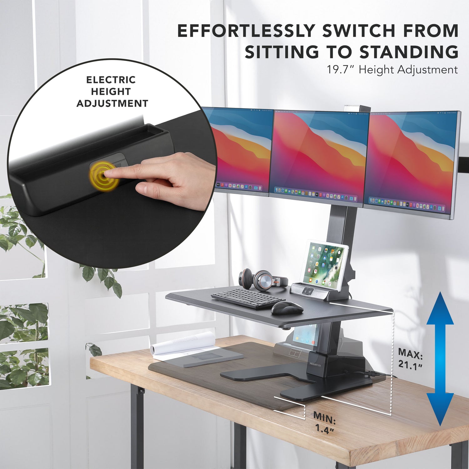 Electric height adjustable desk converter on a desk with multiple monitors and office accessories.