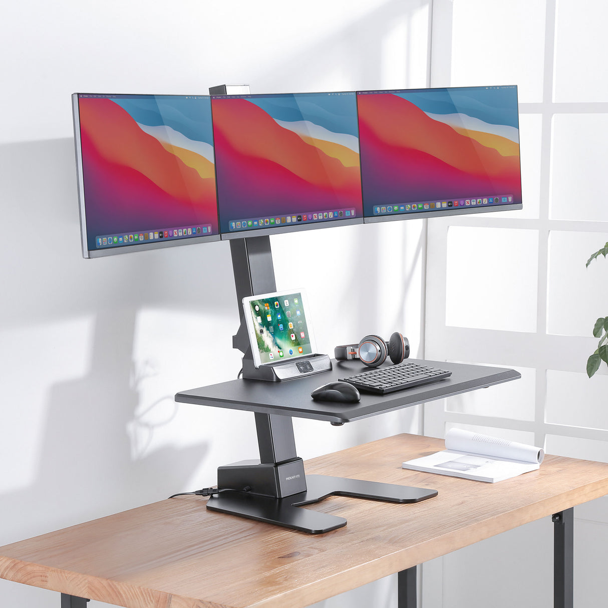 Electric Standing Desk Converter for 3 Monitors Wooden desk with a height-adjustable desk converter and three computer monitors on a white background