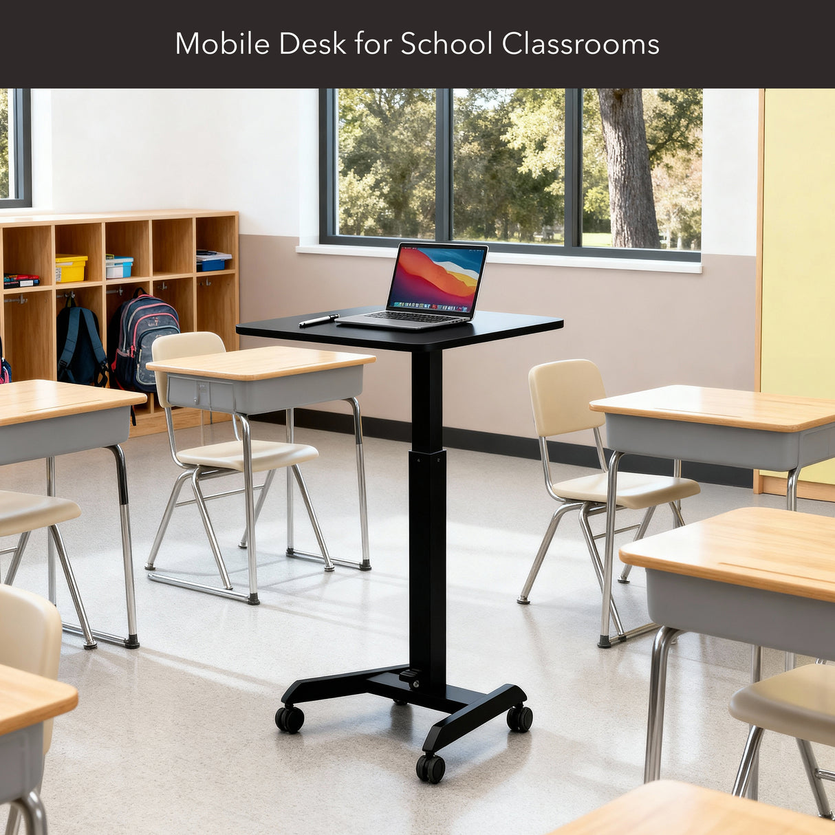 A modern classroom has desks and chairs, with a Mount-It! Height Adjustable Rolling Laptop Desk holding an open laptop. Sunlight streams through large windows in the background.