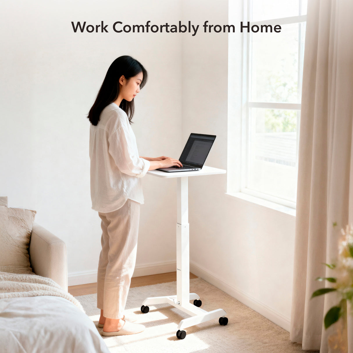 A woman uses a Mount-It! Height Adjustable Rolling Laptop Desk in a bright, minimal room as sunlight streams through the window. Text above her reads, "Work Comfortably from Home.