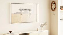 A minimalist living room with a low white TV stand, decor, and a wall-mounted TV bracket framed as art. A vintage clock hangs on the wall, and a cushion and ball are on the wooden floor.