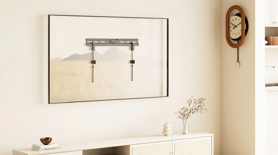A minimalist living room with a low white TV stand, decor, and a wall-mounted TV bracket framed as art. A vintage clock hangs on the wall, and a cushion and ball are on the wooden floor.