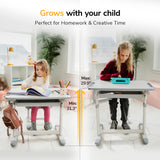 Two girls use the Mount-It! Kids Desk and Chair Set for Ages 3-10 in a bright room. One colors while the other uses a tablet on the tilting desktop, with heights adjustable from 21.3 to 29.9 inches.