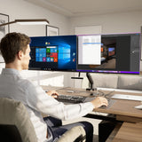 A person works at a desk in a modern office using two monitors mounted on the Mount-It! Dual Monitor Mount with Gas Spring Arm and Crossbar, displaying Windows and photo editing software, with a keyboard, mouse, and tidy workspace.