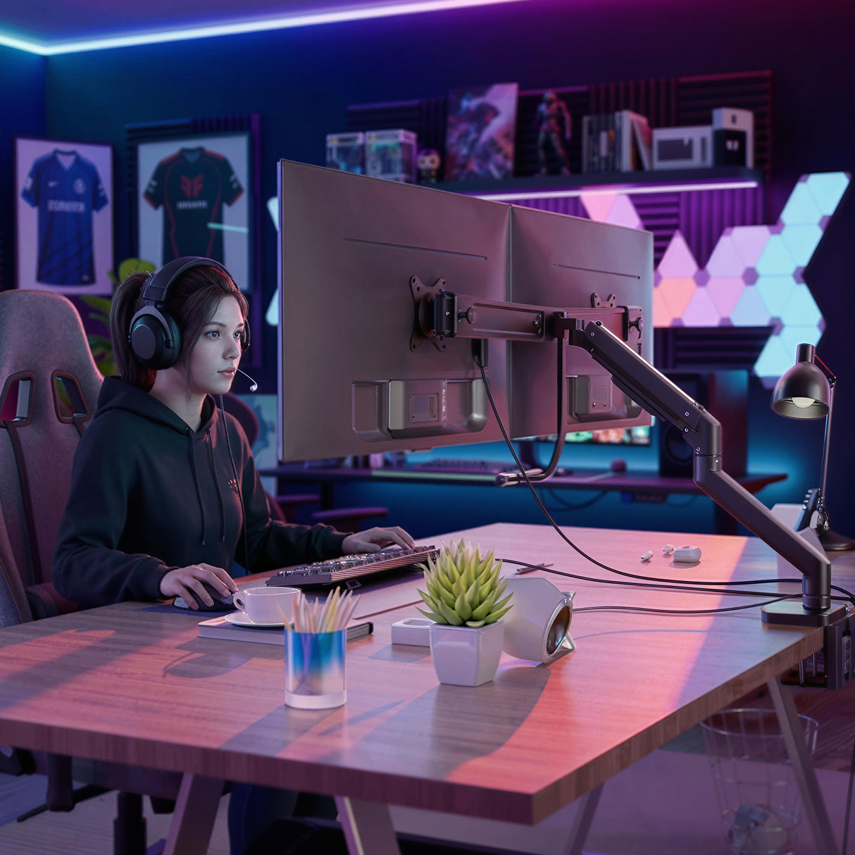 A woman wearing headphones sits at a modern desk featuring the Mount-It! Dual Monitor Mount with Gas Spring Arm and Crossbar, surrounded by gaming accessories, LED lights, and vibrant decor for a colorful, tech-focused vibe.