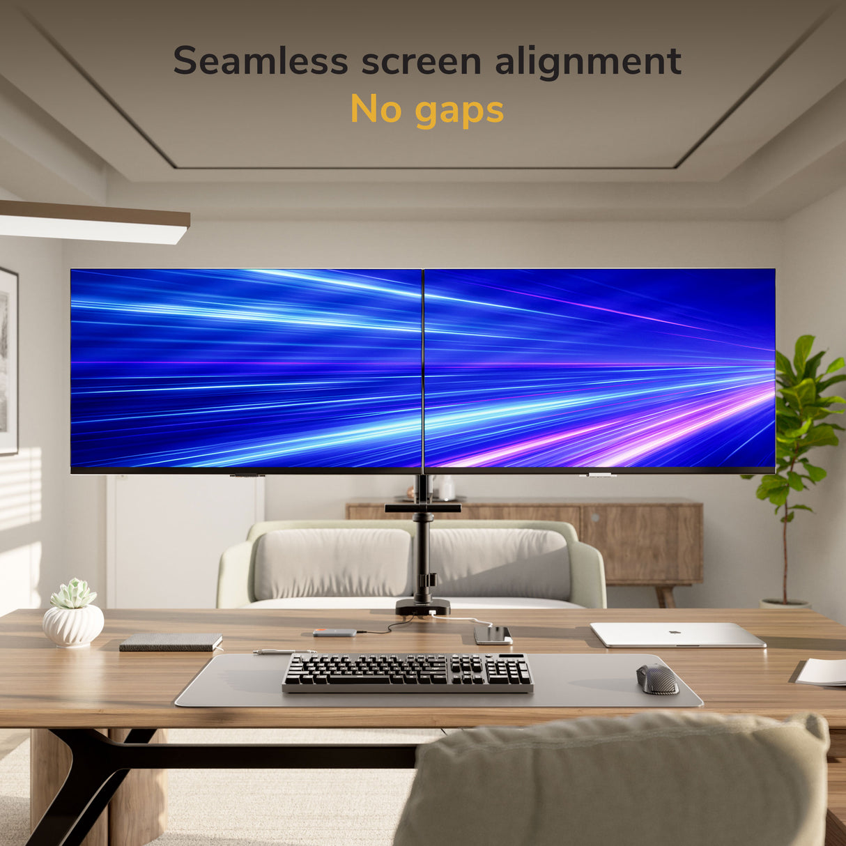 A modern office features two large monitors side by side on the Mount-It! Dual Monitor Mount with Pole and Crossbar, displaying a seamless blue and purple light streak background. Text above reads “Seamless screen alignment, No gaps.”.