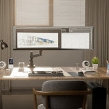 A modern workspace features a large curved monitor on the Mount-It! Heavy-Duty Monitor Mount with Gas Spring Arm, along with a keyboard, mouse, lamp, plant, speakers, and smartphone on a sunlit wooden desk by window blinds.