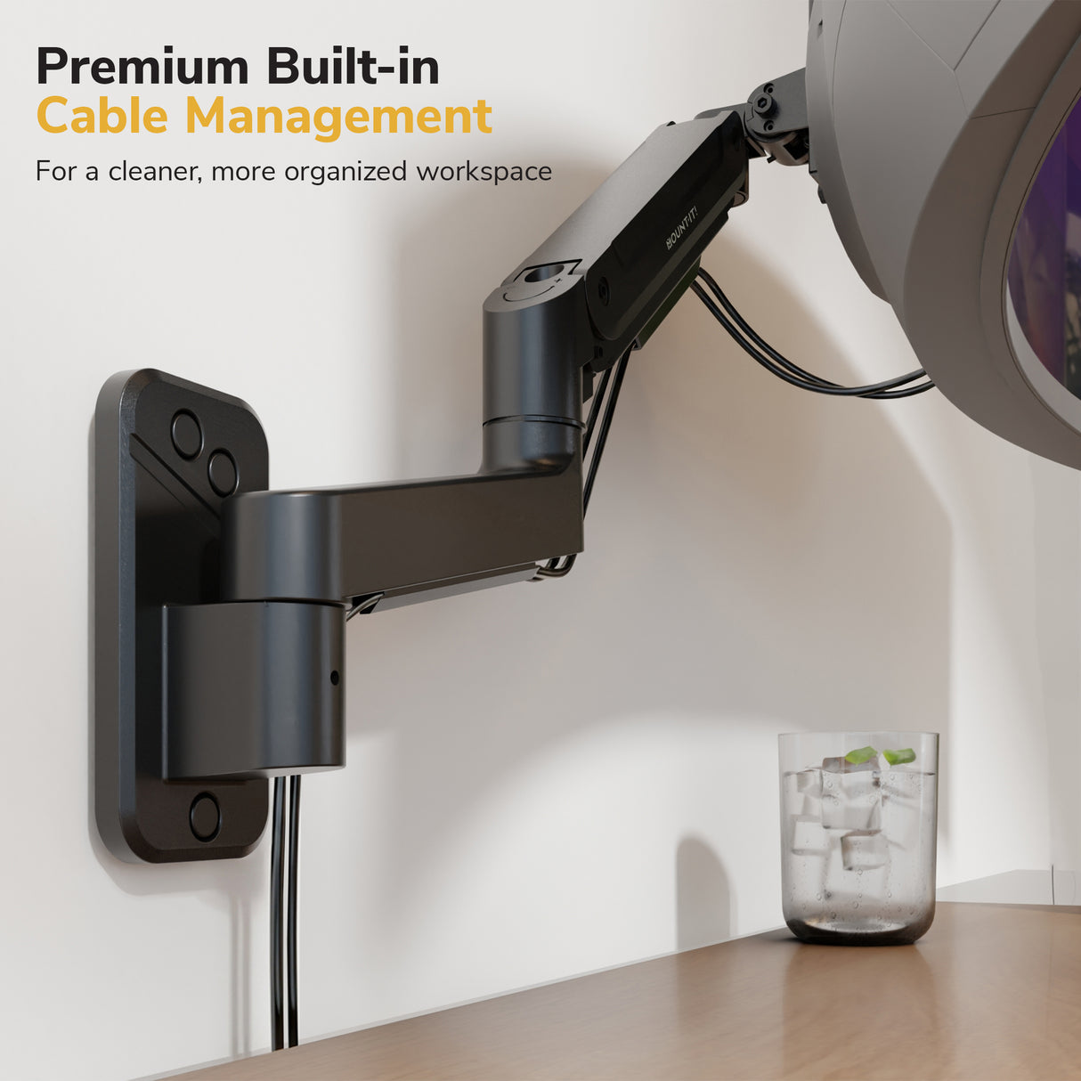 The Mount-It! Heavy-Duty Single Monitor Wall Mount features premium built-in cable management to keep cables organized above your desk for an ergonomic workspace. A glass of ice water rests below. Text reads: Premium Built-in Cable Management.