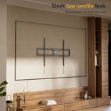 A modern living room features the Mount-It! Heavy-Duty XXL Fixed TV Wall Mount installed above a wooden cabinet. The empty mount sits just 1.3" from the wall, offering a sleek low-profile look.