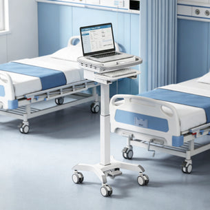 The Mount-It! MedHub Compact Mobile Workstation with locking casters and an adjustable laptop mount stands between hospital beds, adding convenience and modern style to a clean, bright hospital room.