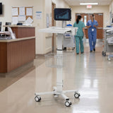 The Mount-It! MedHub Mobile Cart with Tablet Mount stands in a hospital hallway displaying a bar graph. Two healthcare workers in scrubs walk away, and an empty nurses' station is visible to the left.
