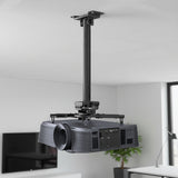The Mount-It! Heavy-Duty Universal Ceiling Projector is mounted on an adjustable bracket in a modern, bright room with white walls and a TV in the background.