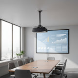 A modern conference room with a long wooden table, gray chairs, large windows, and a Mount-It! Heavy-Duty Universal Ceiling Projector projecting charts onto a wall screen. A plant decorates the windowsill.