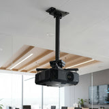The Mount-It! Heavy Duty Projector Ceiling Mount in black securely holds a projector in a modern office conference room featuring glass walls, wood accents, and a large screen.