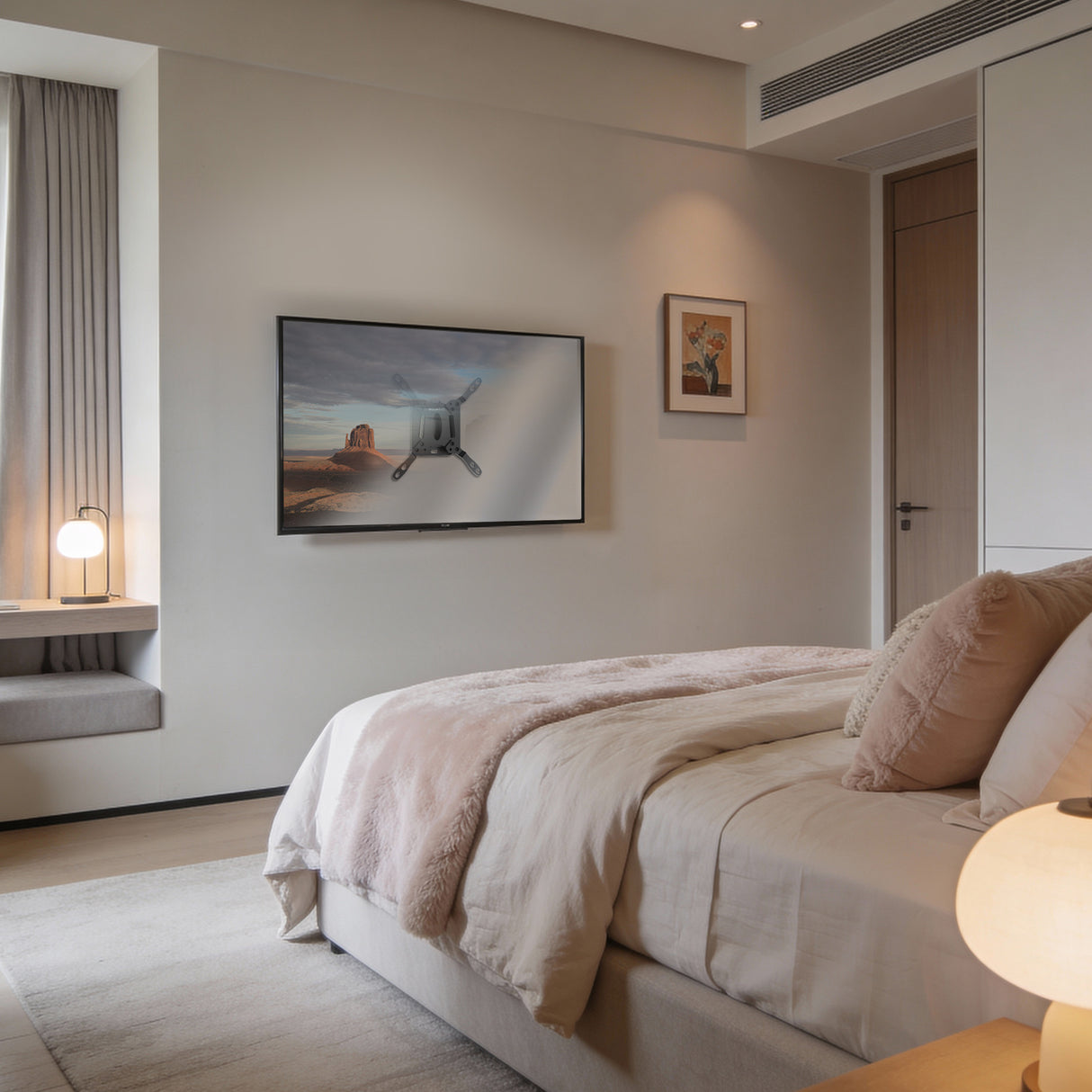 A modern, cozy bedroom with a neatly made bed, soft beige bedding, a Mount-It! Low-Profile TV Wall Mount, a window seat, a small round lamp, minimalist decor, and warm natural light filling the room.