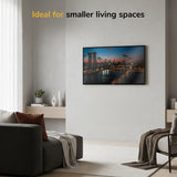 Modern living room with a Mount-It! Low-Profile TV Wall Mount displaying cityscape at sunset, cozy gray sofa, light curtains, and minimalist decor. Top text: Ideal for smaller living spaces.