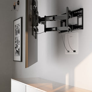 A wall-mounted TV extends on an adjustable bracket above a light wood cabinet with recessed storage. Cables are neatly routed to a Mount-It! In-Wall Media Box (Small), while a black-and-white photo hangs on the adjacent wall.