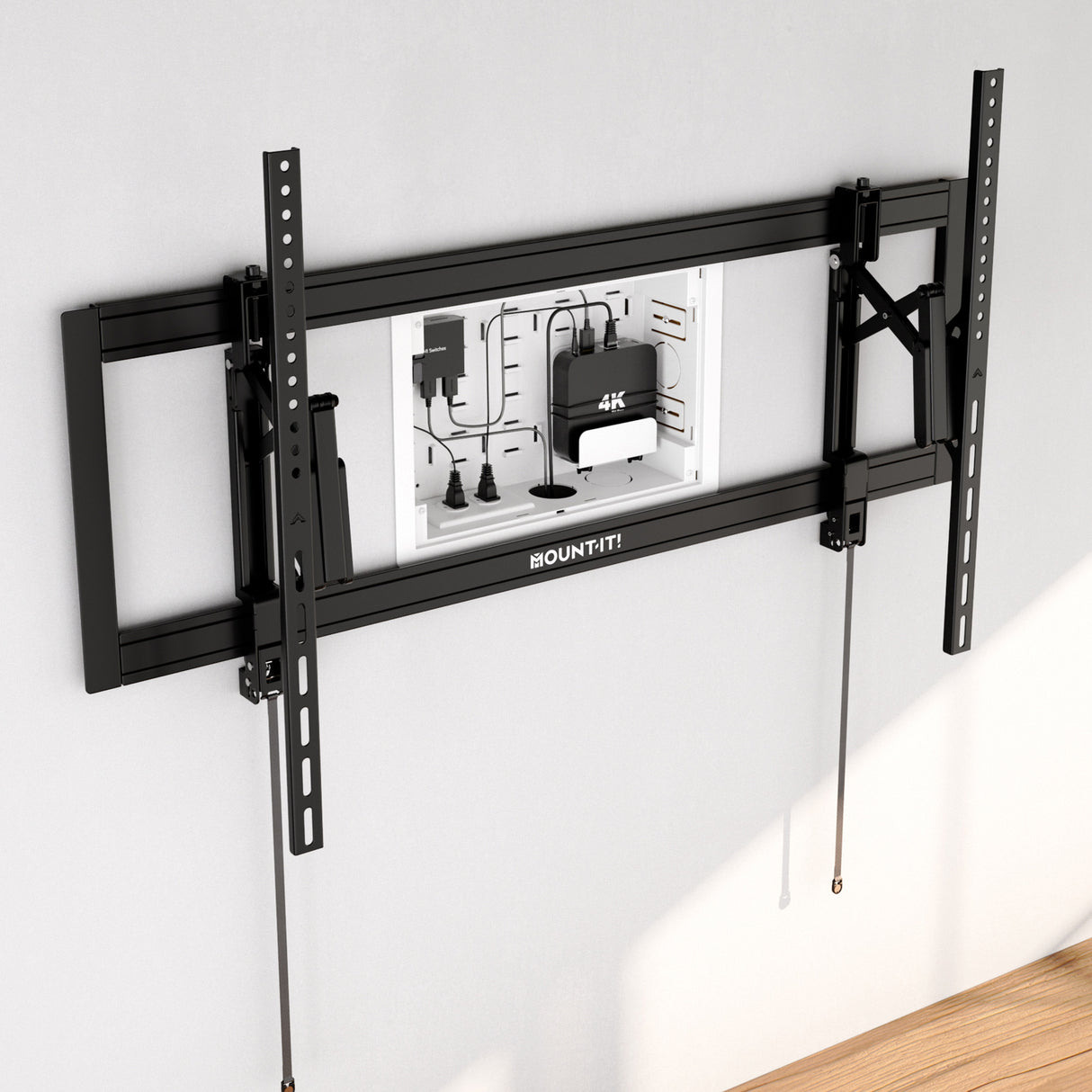 A Mount-It! In-Wall Media Box - Small is installed on a light gray wall above a wooden floor, featuring an open panel that reveals cables, outlets, and a 4K device for discreet equipment storage behind the TV.