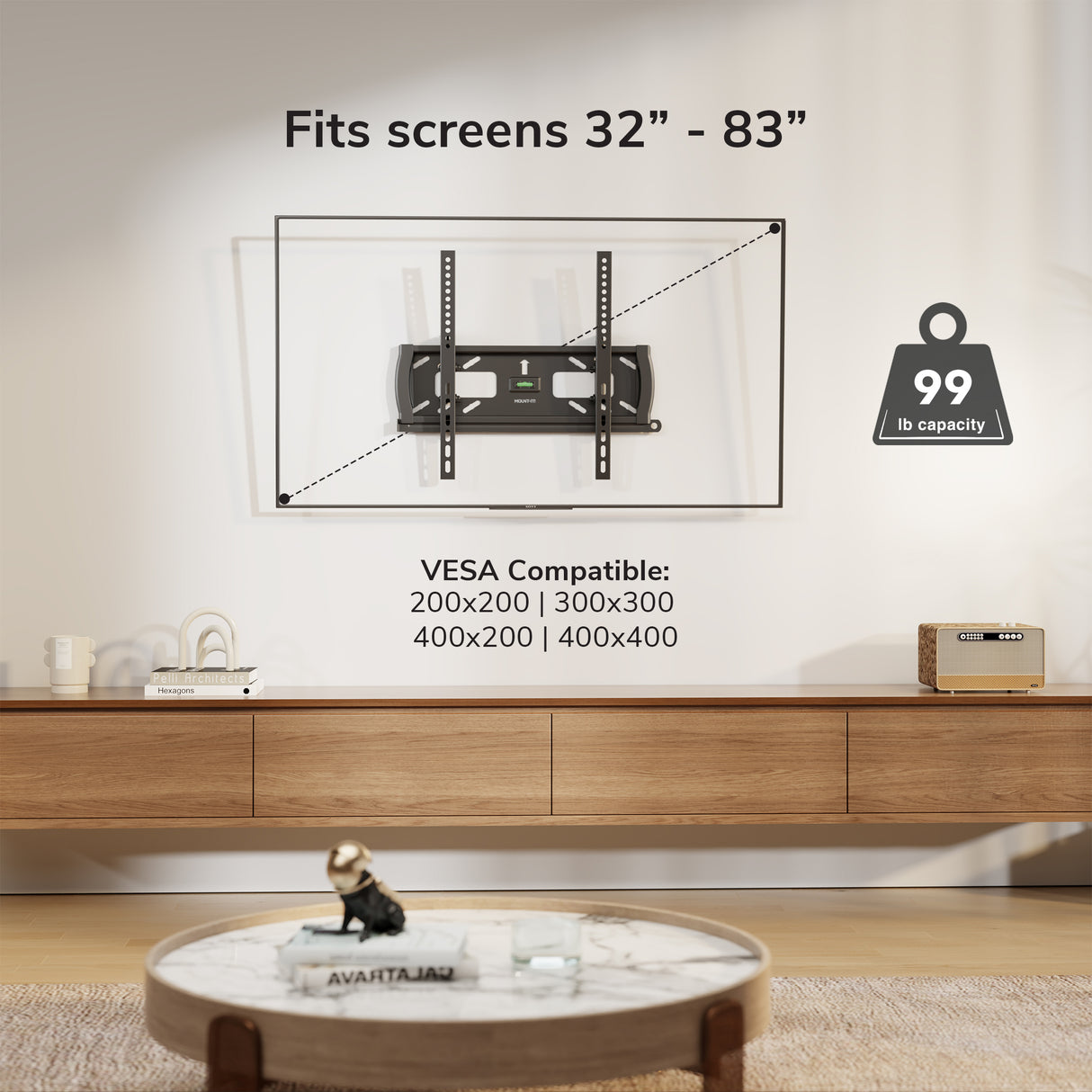 The Mount-It! Locking Anti-Theft TV Wall Mount is installed above a wooden console in a modern living room. It fits 32-83" screens, supports up to 99 lbs, and is VESA 400x400 compatible. A round coffee table sits in the foreground.