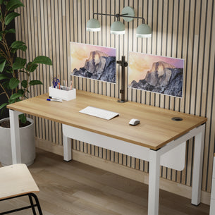 A modern desk setup features the Mount-It! Full Motion Dual Monitor Desk Mount displaying a mountain scene, alongside a keyboard, mouse, desk organizer with pens, three-bulb lamp, potted plant, and wooden chair against a slatted wood wall.