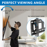 A person adjusts the Mount-It! Heavy-Duty Tilt TV Wall Mount, showing its +10° to -12° tilt range. An inset highlights the tilt adjustment knob, and text notes reduced glare by tilting this VESA compatible mount.