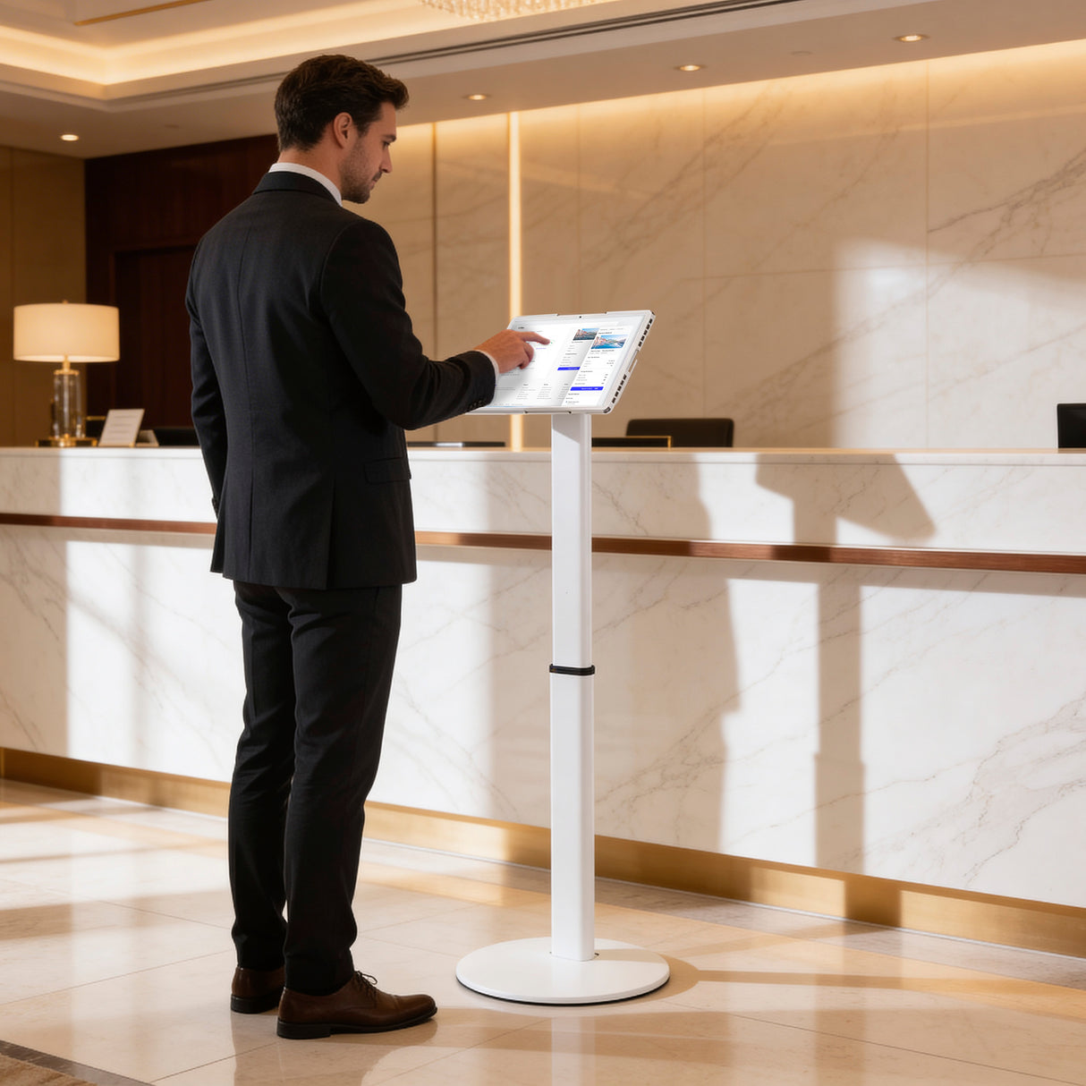 A man in a suit uses the Mount-It! Universal Tablet Floor Kiosk in a bright hotel lobby with a marble reception desk in the background.