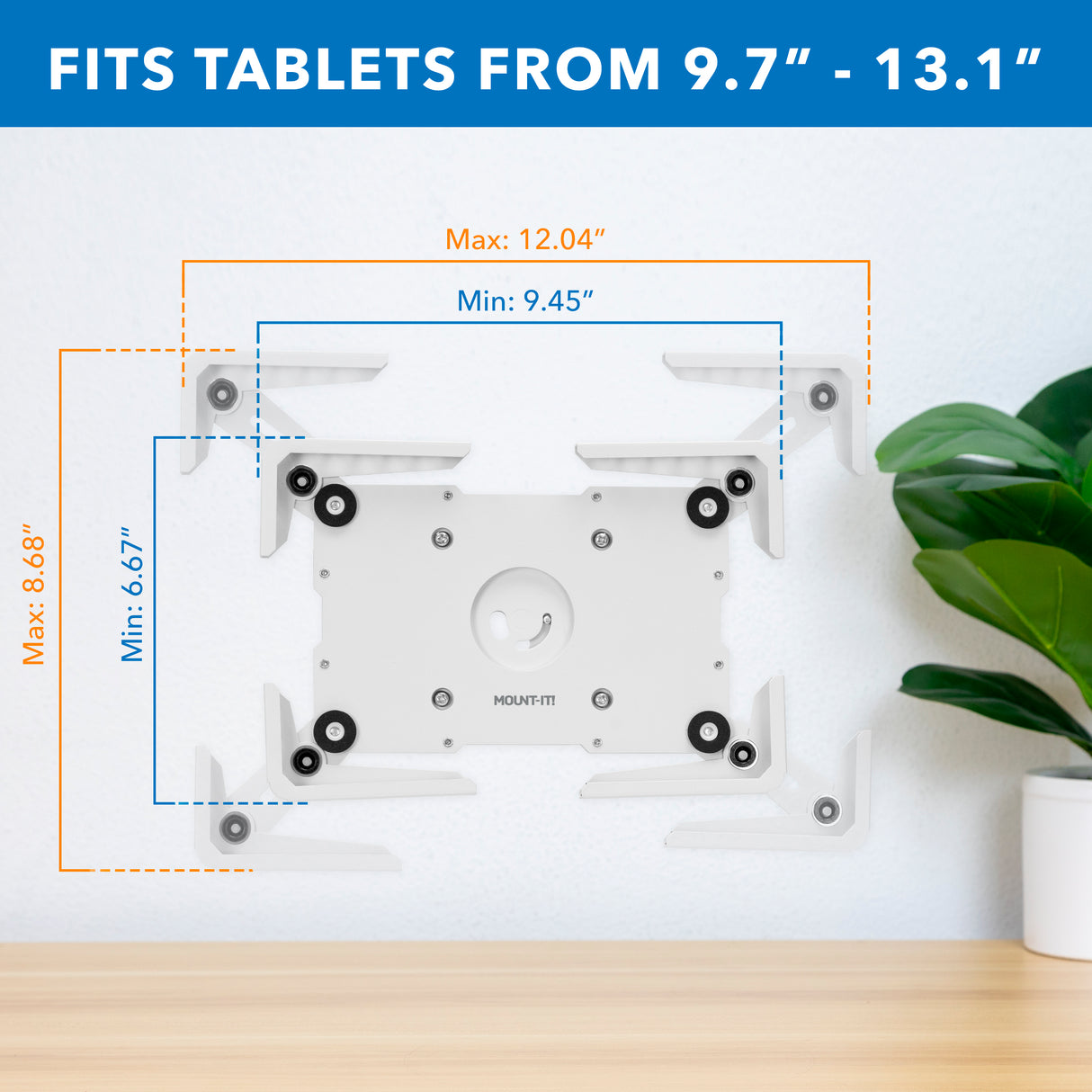The Mount-It! Universal Tablet Wall Mount, with labeled dimensions, securely fits 9.7–13.1 inch tablets in an enclosure and is shown above a wooden desk with a green plant on the right.