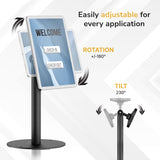 Universal Anti-Theft Tablet Countertop Stand by Mount-It! shown with adjustable rotation and tilt features, demonstrating 180-degree swivel and 230-degree tilt capabilities on a sleek, black cylindrical stand with a round base. The image highlights the stand’s ease of adjustment for optimal tablet positioning in various applications while securely holding a tablet with a welcome screen in a professional, modern setting.