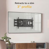 A Mount-It! Full-Motion TV Wall Mount with 40" Extension is installed above a white console on a light wall. Text above says “Retracts to a slim 3" profile” in black and yellow. Features tilt and swivel for perfect viewing.