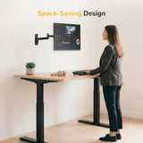 A woman stands at her desk, adjusting her monitor mounted on the Mount-It! Full Motion Display Wall Mount.
