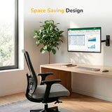A modern home office features a wooden desk, ergonomic chair, large window, and the Mount-It! Full Motion Display Wall Mount holding a monitor with a spreadsheet. Wireless keyboard, mouse, and potted plant included. Text: "Space Saving Design.