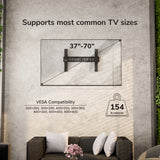 The Mount-It! Pop-Out Video Wall Mount fits 37–70" TVs, supports up to 154 lbs, and allows precise alignment with various VESA sizes. Shown mounted above a gray couch with white pillows and a pink flower arrangement.