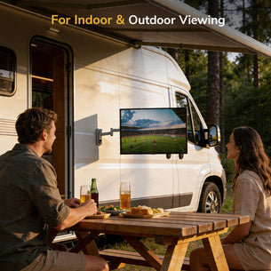 A man and woman sit at a picnic table outside a camper van, watching soccer on a TV mounted with the Mount-It! Full Motion Lockable RV and Trailer TV Mount. Drinks and snacks are on the table, and trees fill the outdoor background.