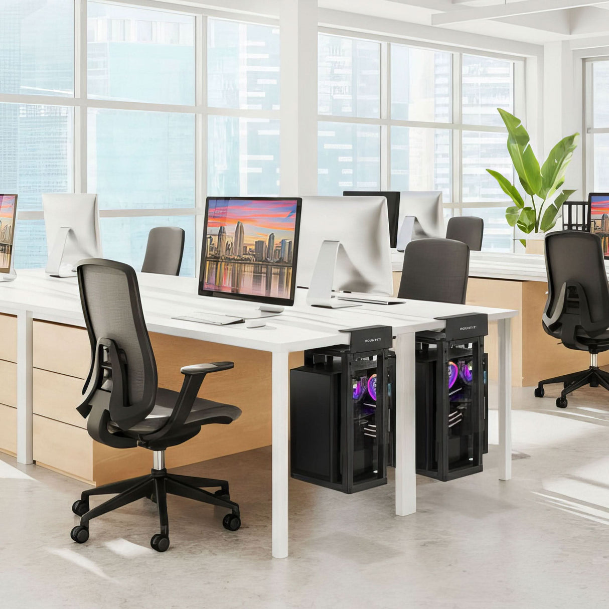 A modern, bright office with large windows, sleek desks, black office chairs, desktop computers in Mount-It! Heavy-Duty Clamp-On CPU Mounts with purple lighting under the desks, and a green plant in the corner.