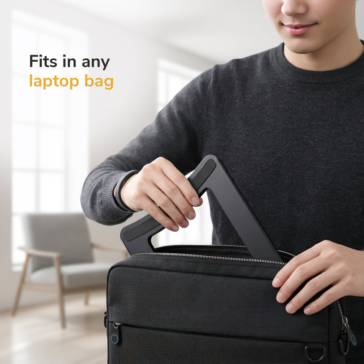 A person in a dark sweater slips the Mount-It! Portable Folding Laptop Stand into a black laptop bag. Text on the image says, “Fits in any laptop bag,” set against a bright, modern room.