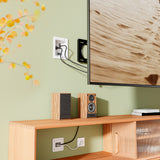 A wall-mounted TV with visible cables and a white wall plate above a wooden shelf housing speakers and an audio receiver could look neater by using the Mount-It! In-Wall Cable Management Kit with USB for improved cable organization.